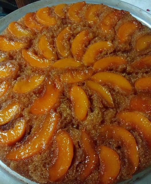 A golden peach upside-down cake with caramelized peaches on top, served on a large platter.